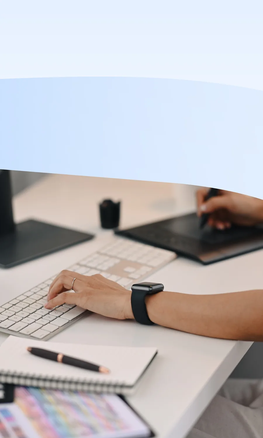Clavier et tablette graphique sous les mains, bureau clair avec carnet, stylo et nuancier